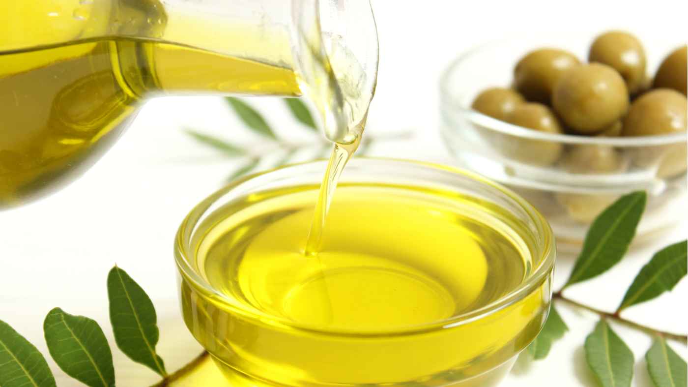 Olive oil being poured into bowl with bowl of olives in the background
