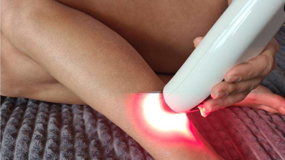 Woman using a red light device on her lower leg